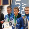 Na zdjęciu trzech zawodników HKS Azymut Mochy, którzy stoją na podium i pozują do zdjęcia z medalami i dyplomami.