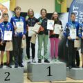 Wspólne zdjęcie zawodników na podium. Zawodnicy pozują z medalami oraz dyplomami.