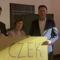 Na zdjęciu trójka nauczycieli trzymająca baner z napisem "czek".