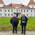 Na zdjęciu dwóch seniorów pozujących na tle pałacu w Buczu.