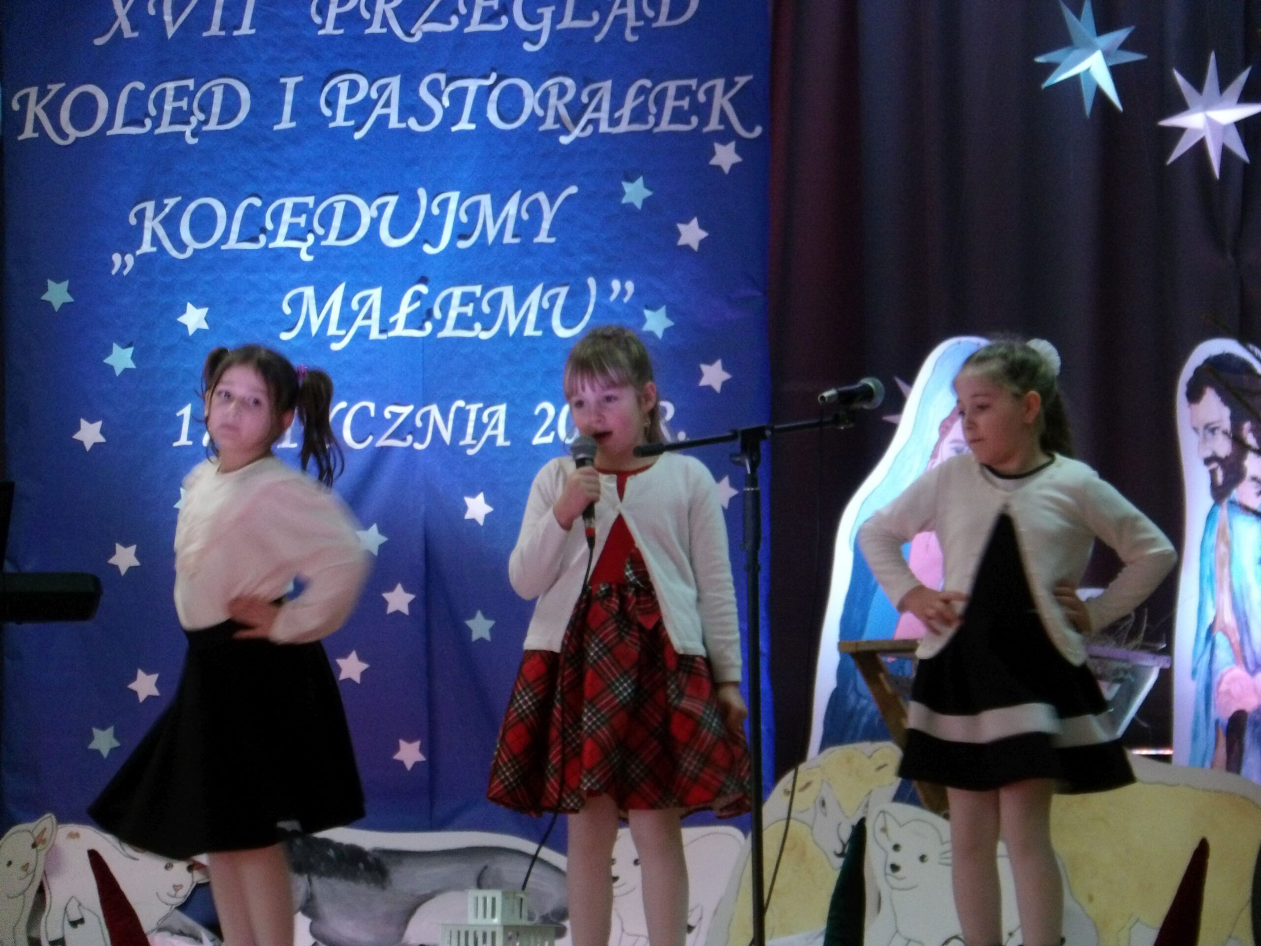 Zdjęcie przedstawia trzy dziewczynki, które śpiewają na scenie.
