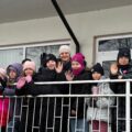 Zdjęcie przedstawia dzieci wraz z opiekunem uśmiechający się i machający do zdjęcia.