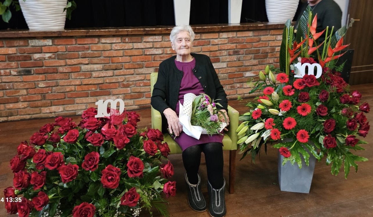 Na zdjęciu jubilatka siedząca wśród bukietów róż w sali GCKiB.