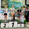 Zdjęcie przedstawia trójkę dziewcząt stojących na podium. Każda z nich ma puchar. Koło dziewczynek stoi Pani Elżbieta Wita oraz Pani Dyrektor.