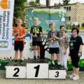 Zdjęcie przedstawia trójkę chłopców stojących na podium. Każdy z nich ma puchar oraz medal. Koło chłopców stoi Pani Elżbieta Wita oraz Pani Dyrektor.