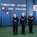 Na zdjęciu dh Józef Pauch, dh Marian Skibiński oraz dh Henryk Żok. Wyżej wymienieni pozują na tle ścianki, na której widnieje napis: "Powiatowe obchody dnia strażaka"