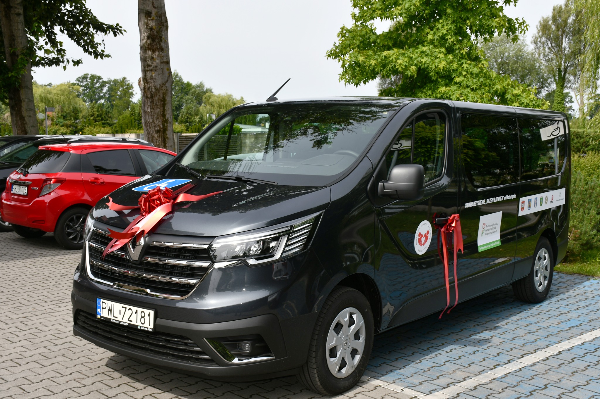 Na zdjęciu czarny bus Renault Trafic z 2024 roku. Bus ozdobiony czerwonymi kokardami.