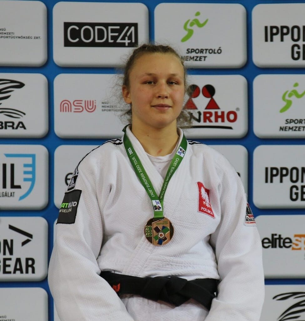 Na zdjęciu Martyna Skorupińska stojąca na podium z medalem. Dziewczyna ubrana jest w judogę z czarnym pasem.
