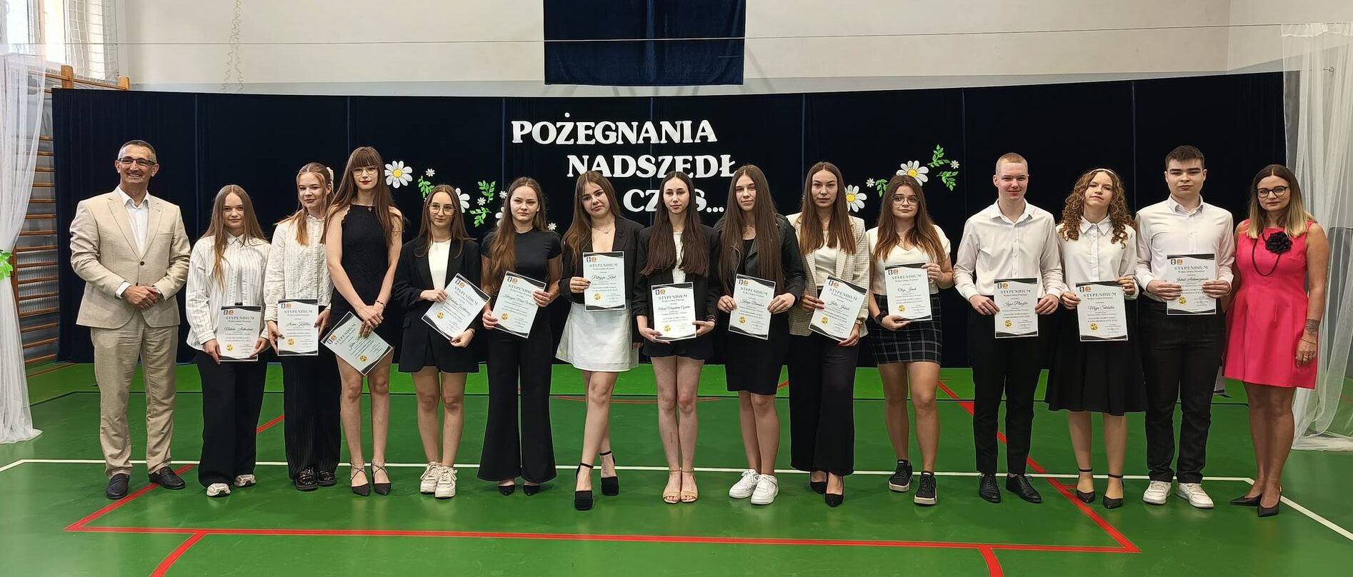 Grupowe zdjęcie uczniów ze szkoły ponadpodstawowej w Przemęcie wraz z wójtem oraz dyrektorem Katarzyną Wiśniewską. Zdjęcie wykonano na sali gimnastycznej w szkole.