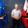 Na zdjęciu wójt składający podziękowanie dla byłego sołtysa Starkowa. Na fotografii także przewodnicząca rady gminy, która trzyma różę. W tle ścianka oraz flagi.