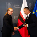 Na zdjęciu uchwycono moment uścisku dłoni wójta wraz z byłym sołtysem Perkowa. W tle ścianka oraz flagi.