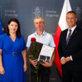 Na zdjęciu wójt wraz z przewodniczącą rady oraz byłym sołtysem Górska, który trzyma róże wraz podziękowaniami oraz dobrym upominkiem. W tle ścianka oraz flagi.