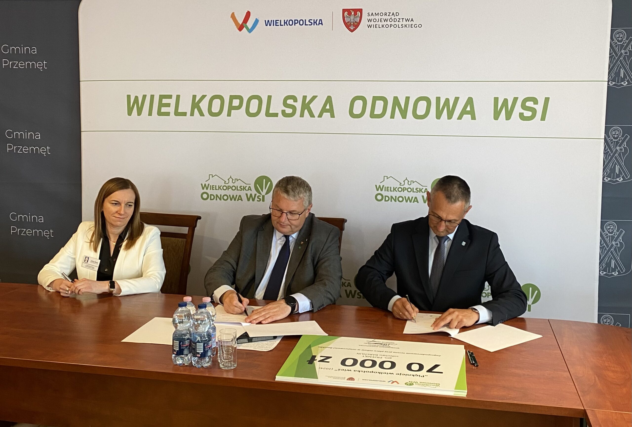 Zdjęcie przedstawia moment podpisywania umowy przez wicemarszałka Województwa Wielkopolskiego Krzysztofa Grabowskiego, wójta Gminy Przemęt Janusza Frąckowiaka oraz głównego księgowego Alicję Bautę. W tle ścianka "Wielkopolska Odnowa Wsi".