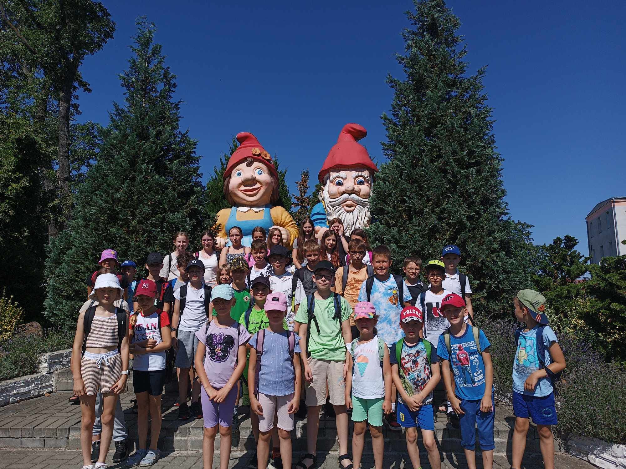 Grupowe zdjęcie dzieci w Parku Krasnala. W tle duże krasnale ogrodowe.
