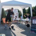 Na zdjęciu stoisko siłowni "RAMPA". Na fotografii znajduje się dwójka trenerów. Przy stoisku znajdują się m.in. leżaki, sprzęt do siłowni oraz produkty z cateringu dietetycznego.