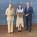 Na zdjęciu wójt, zastępca dyrektora GCKiB oraz jedna z nagrodzonych mażoretek. Wszyscy pozują na tle ścianki gmina Przemęt, która zawiera herb gminy.