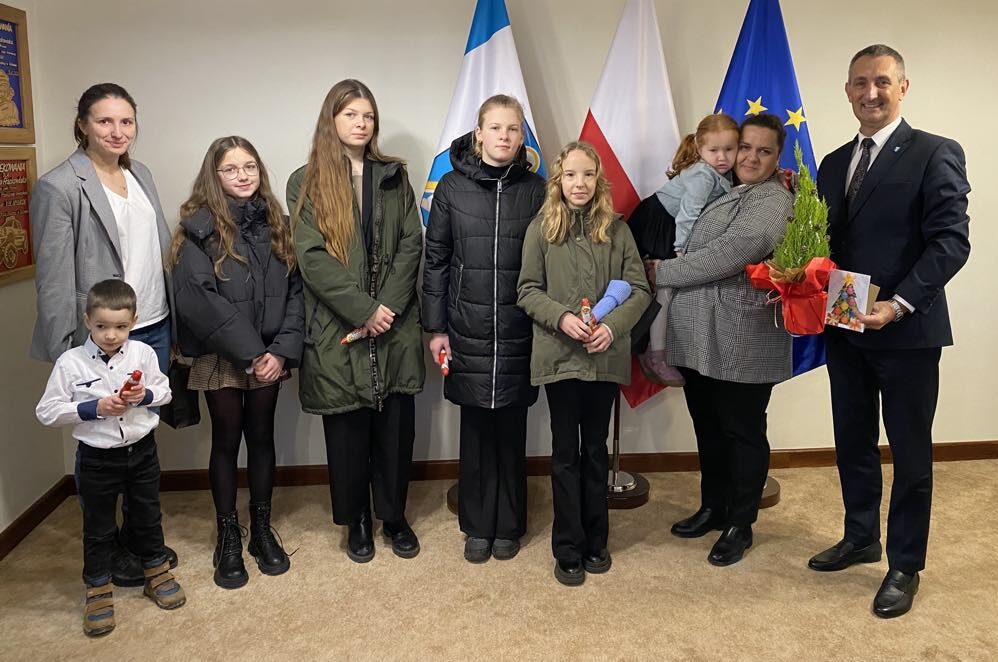 Wspólne zdjęcie wójta wraz z dyrektorką szkoły w Starkowie Lidią Ławecką, nauczycielką szkoły oraz uczniami. Wójt trzyma małą świąteczną choinkę i kartkę świąteczną, a uczniowie trzymają czekoladowe gwiazdorki.