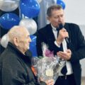 Na zdjęciu Pan Robert Szwed przemawia przez mikrofon. Koło niego stoi jeden z uczestników trzymając nagrodę.