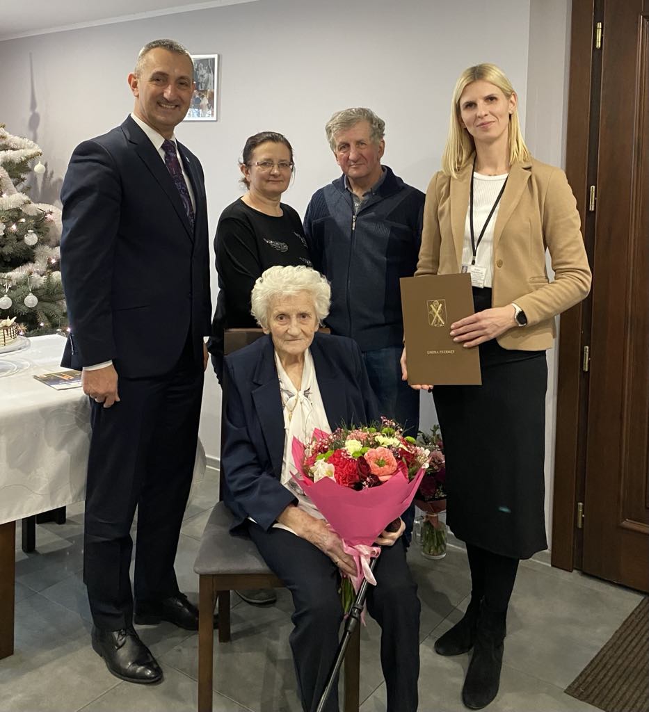 Na zdjęciu wójt Janusz Frąckowiak, pracownik urzędu stanu cywilnego w Przemęcie pani Irena oraz jubilatka Eleonora i dwójka jej bliskich osób. Pani Eleonora trzyma bukiet kwiatów.