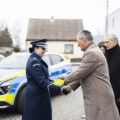Na zdjęciu wójt oficjalnie przekazuje samochód komendant Katarzynie Sobczyk-Kukawce. Wyżej wymienieni podają sobie dłonie. W tle nowy radiowóz oraz inne osoby obecne na uroczystości.