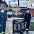 Na zdjęciu dwójka chłopaków z OSP Mochy. Stoją oni po obu stronach tablicy pamiątkowej, na której wypisane są nazwiska powstańców.