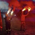 Na zdjęciu widoczne dwie osoby trzymające race dymne, z których wydobywa się biały i czerwony dym.