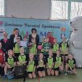 Grupowe zdjęcie zawodników z Moch wraz z opiekunami i osobą przebraną za białego misia. Zawodnicy mają założone medale, trzymają dyplom, puchar oraz nagrody w postaci piłek. W tle plakat z napisem Gminny Turniej Sportowy Biały Miś oraz winder Honorowy Patronat Wójta Gminy Przemęt.