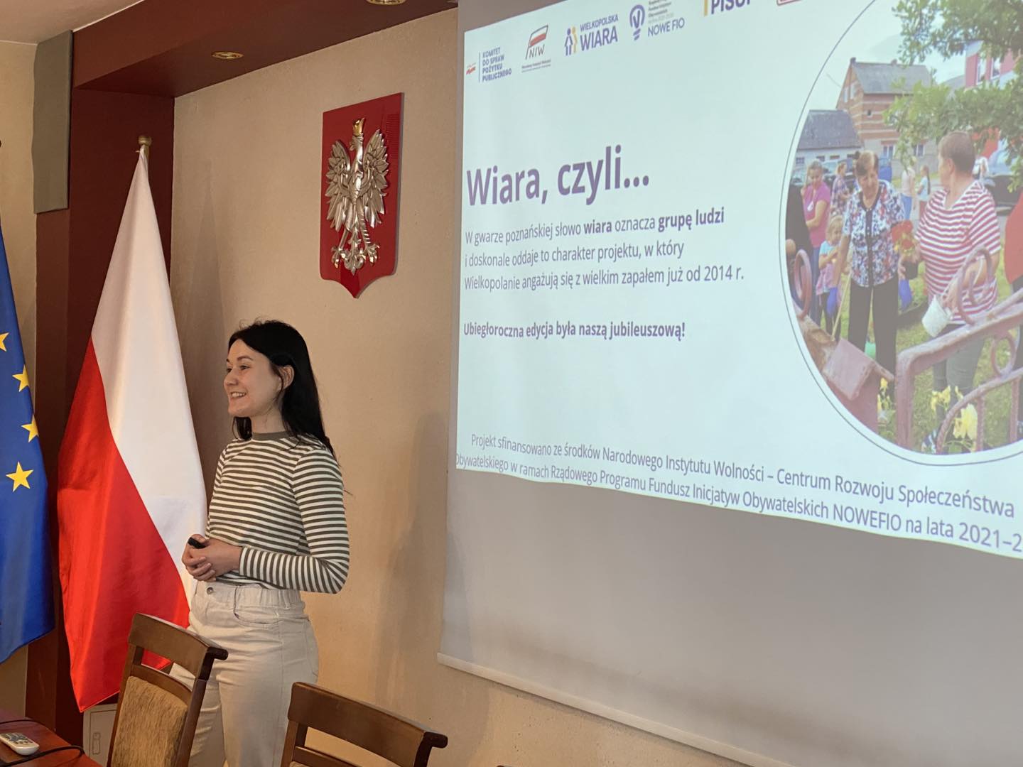 Na zdjęciu Pani Oksana - przedstawicielka PISOP podczas omawiania tematu spotkania. Na projektorze wyświetlana jest informacja: "Wiara, czyli... w gwarze poznańskiej słowo wiara oznacza grupę ludzi i doskonale oddaje to charakter projektu, w który Wielkopolanie angażują się z wielkim zapałem już od 2014 r."