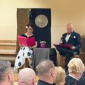 Na zdjęciu występ grupy kabaretowej. Na scenie kobieta i mężczyzna, którzy siedzą przy stoliczku i odgrywają swoje role.