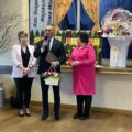Na zdjęciu wójt Janusz Frąckowiak podczas przemowy na Dniu Kobiet w Nowej Wsi. Wójt trzyma list gratulacyjny oraz kwiaty. Koło wójta stoją dwie Panie.