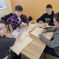 Czworo nastolatków siedzi przy stole i zdobi materiałowej torby.