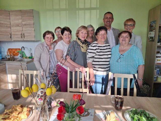 Wspólne zdjęcie, na którym znajduje się wójt, dyrektorka GOPSu oraz członkinie klubu seniora. Na fotografii widoczne są ozdoby wielkanocne znajdujące się na stole.