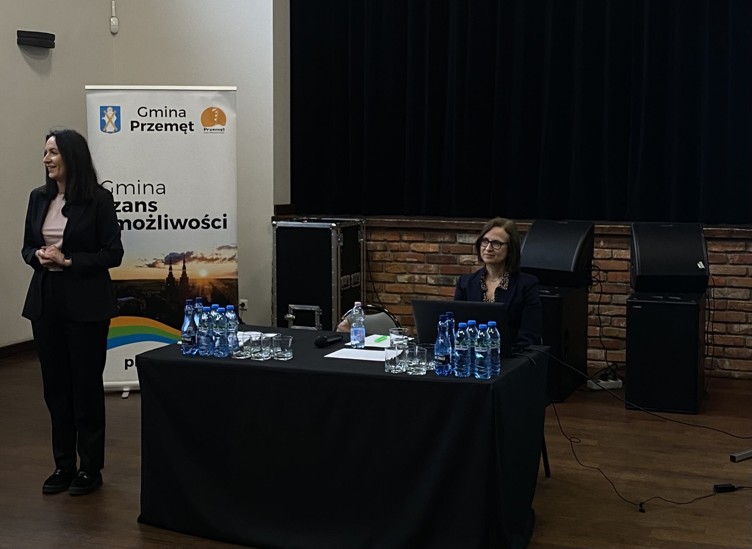 Na zdjęciu Patrycja Pabich - radna powiatu wolsztyńskiego podczas powitania osób przybyłych na spotkanie. Na fotografii także Anna Maluśka radca prawny. W tle roll up Gminy Przemęt.