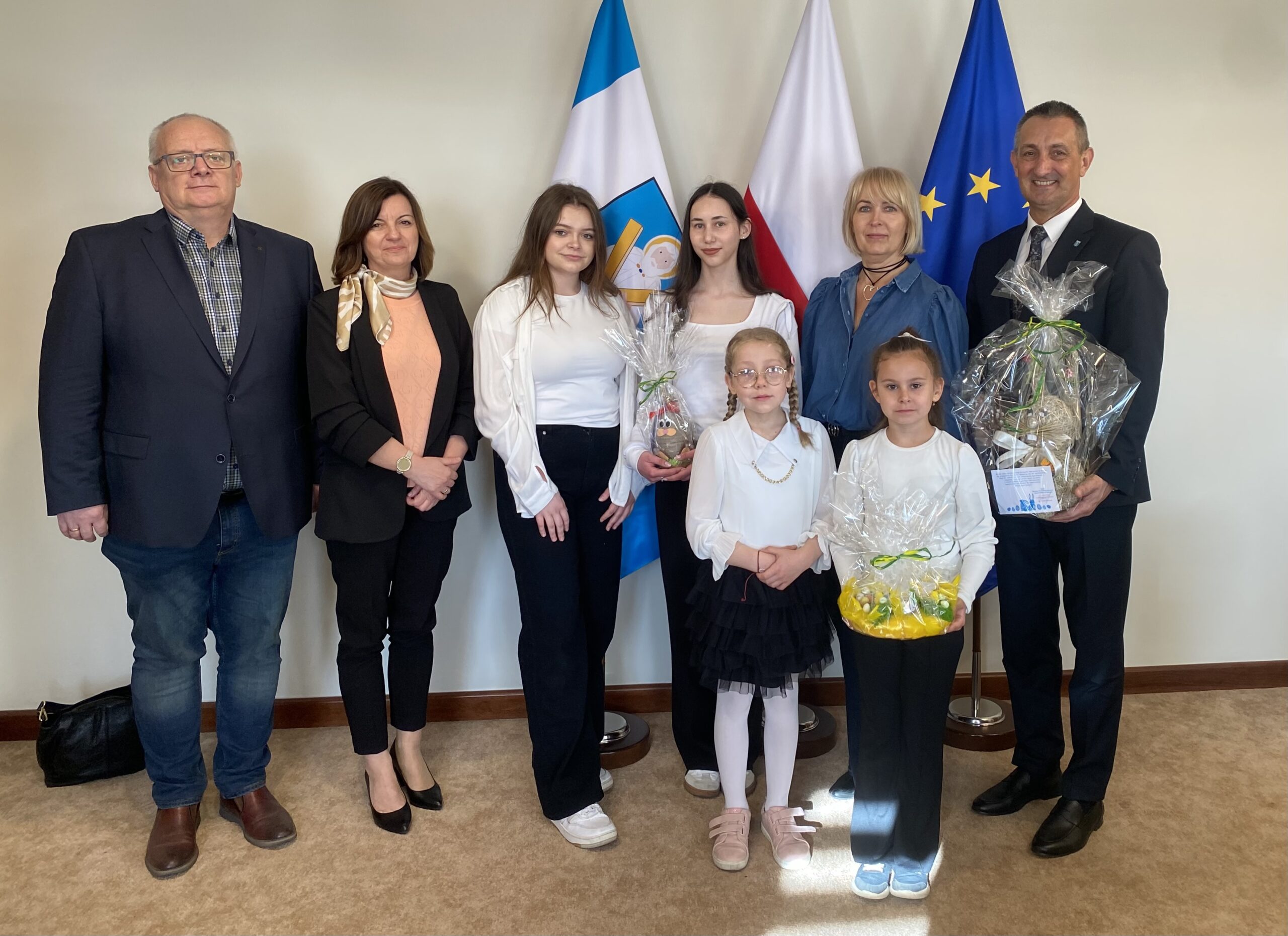 Na wspólnym zdjęciu znajduje się wójt, czwórka uczennic ze szkół z Przemętu, dyrektor zespołu szkół w Przemęcie oraz dwie wicedyrektorki. Wójt trzyma prezent od uczniów - zajączka wielkanocnego. Dwie uczennice również trzymają wielkanocne ozdoby. Zdjęcie wykonano w biurze wójta, w tle flagi: polski, europejska oraz flaga z herbem gminy.