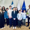 Na wspólnym zdjęciu znajduje się wójt, uczniowie ze szkoły ze Starkowa wraz z nauczycielką oraz Pani Patrycja Pabich z wydziału oświaty. Wójt trzyma wielkanocny prezent od uczniów - kwiatki w doniczce. Zdjęcie wykonano w biurze wójta, w tle flagi: polski, europejska oraz flaga z herbem gminy.