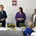 Na zdjęciu wójt gminy, przewodnicząca rady gminy oraz skarbnik gminy. Wójt przemawia do osób obecnych na sali.