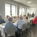 Na zdjęciu seniorzy siedzący przy zastawionym stole. W tle widać wójta oraz dyrektorkę i pracownika GOPSu.