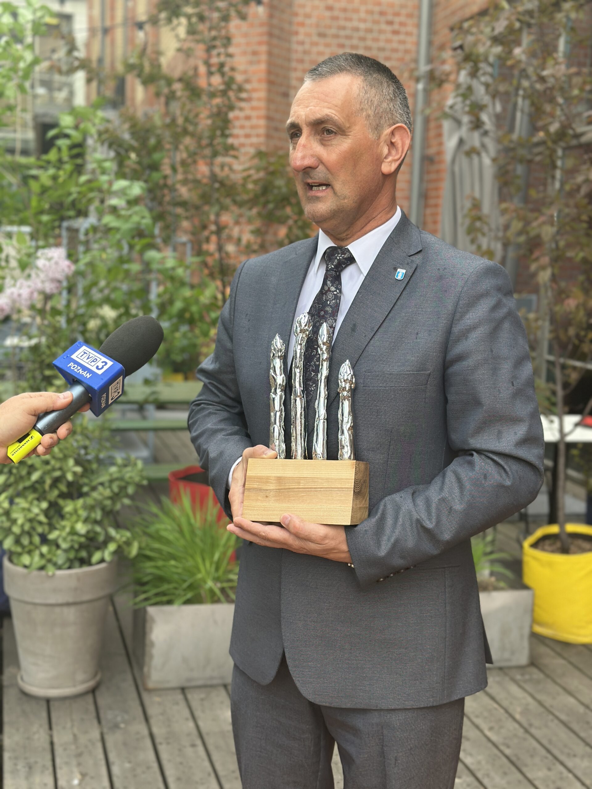Na zdjęciu wójt gminy Janusz Frąckowiak podczas udzielania wywiadu dla TVP 3 Poznań. Wójt trzyma w rękach statuetkę ze srebrnymi szparagami.