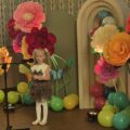 Na zdjęciu dziewczynka podczas swojego wystąpienia. W tle wystrój sceny - kolorowe duże kwiaty i balony.