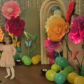 Na zdjęciu dziewczynka podczas swojego wystąpienia. W tle wystrój sceny - kolorowe duże kwiaty i balony.