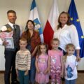 Wspólne zdjęcie zastępcy wójta z czwórką przedszkolaków i dyrektorką przedszkola. Zastępca trzyma w ręce kwiaty i laurkę.