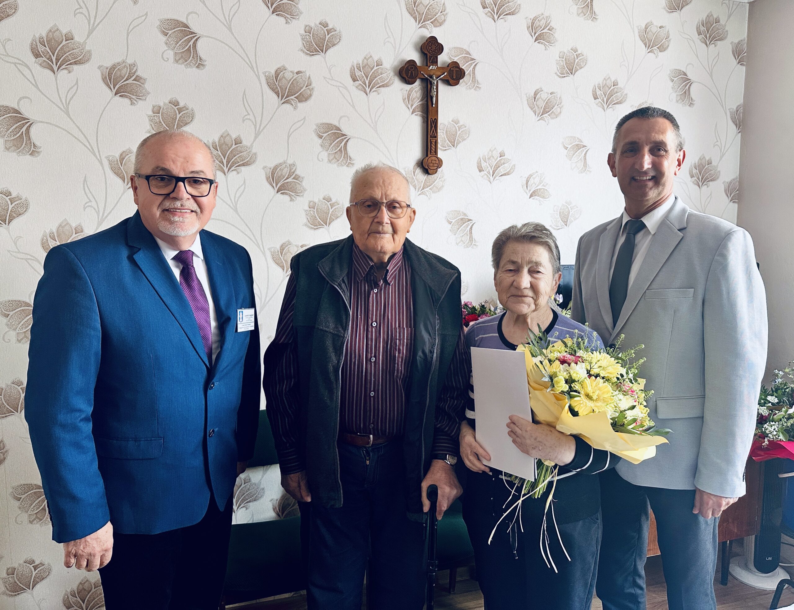 Wspólne zdjęcie państwa Poźniak, wójta oraz kierownika urzędu stanu cywilnego Leszka Anglarta. Pani Monika pozuje do zdjęcia z bukietem kwiatów oraz listem gratulacyjnym.