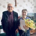 Wspólne zdjęcie państwa Poźniak. Pani Monika trzyma bukiet kwiatów oraz list gratulacyjny.