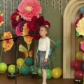 Na zdjęciu dziewczynka podczas swojego wystąpienia. W tle wystrój sceny - kolorowe duże kwiaty i balony.