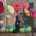 Na zdjęciu chłopiec podczas swojego wystąpienia. W tle wystrój sceny - kolorowe duże kwiaty i balony.
