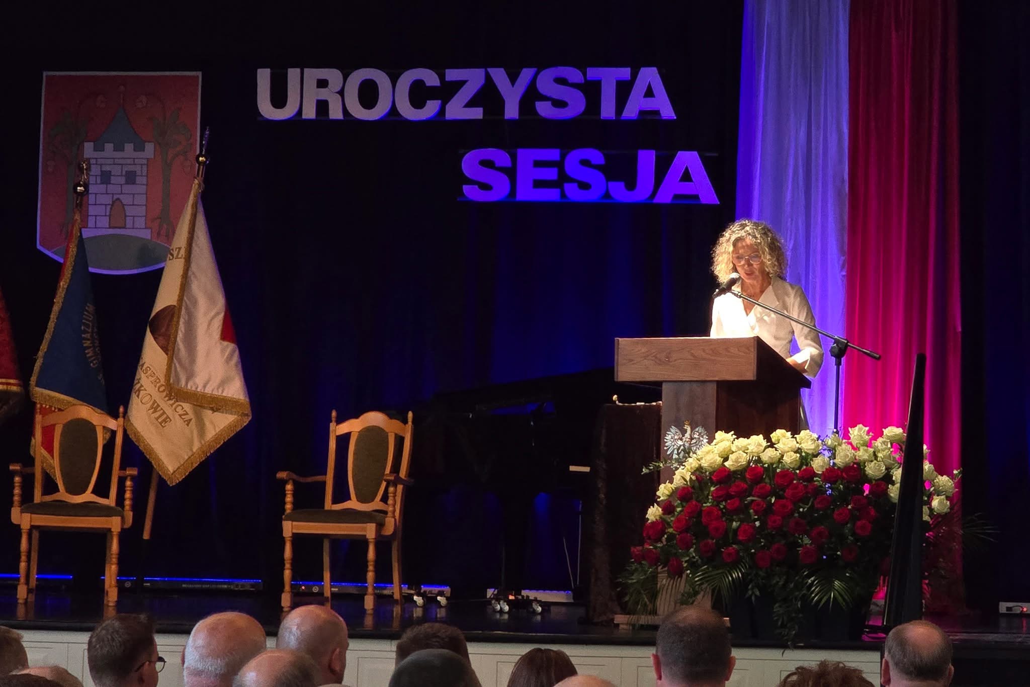 Na fotografii burmistrz Śmigla Małgorzata Adamczak podczas przemowy na scenie. Na scenie przypięto duży napis: "Uroczysta sesja", a obok niego herb miasta Kobylnica