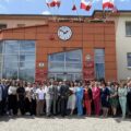 Grupowe zdjęcie wszystkich osób obecnych na sesji absolutoryjnej. Wójt pozuje do zdjęcia z bukietem czerwonych róż. Zdjęcie wykonano przed budynkiem urzędu.