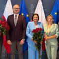 Na zdjęciu wójt, zastępca wójta oraz skarbnik gminy Przemęt. Wyżej wymienione osoby pozują do zdjęcia z bukietami róż. Na zdjęciu znajduje się także delegacja dyrektorów złożona z dyrektor przedszkola z Nowej Wsi i dyrektora szkoły z Bucza. Wszyscy pozują na tle ścianki "Gmina Przemęt" oraz flag: dwóch flag Polski i dwóch Europejskich.