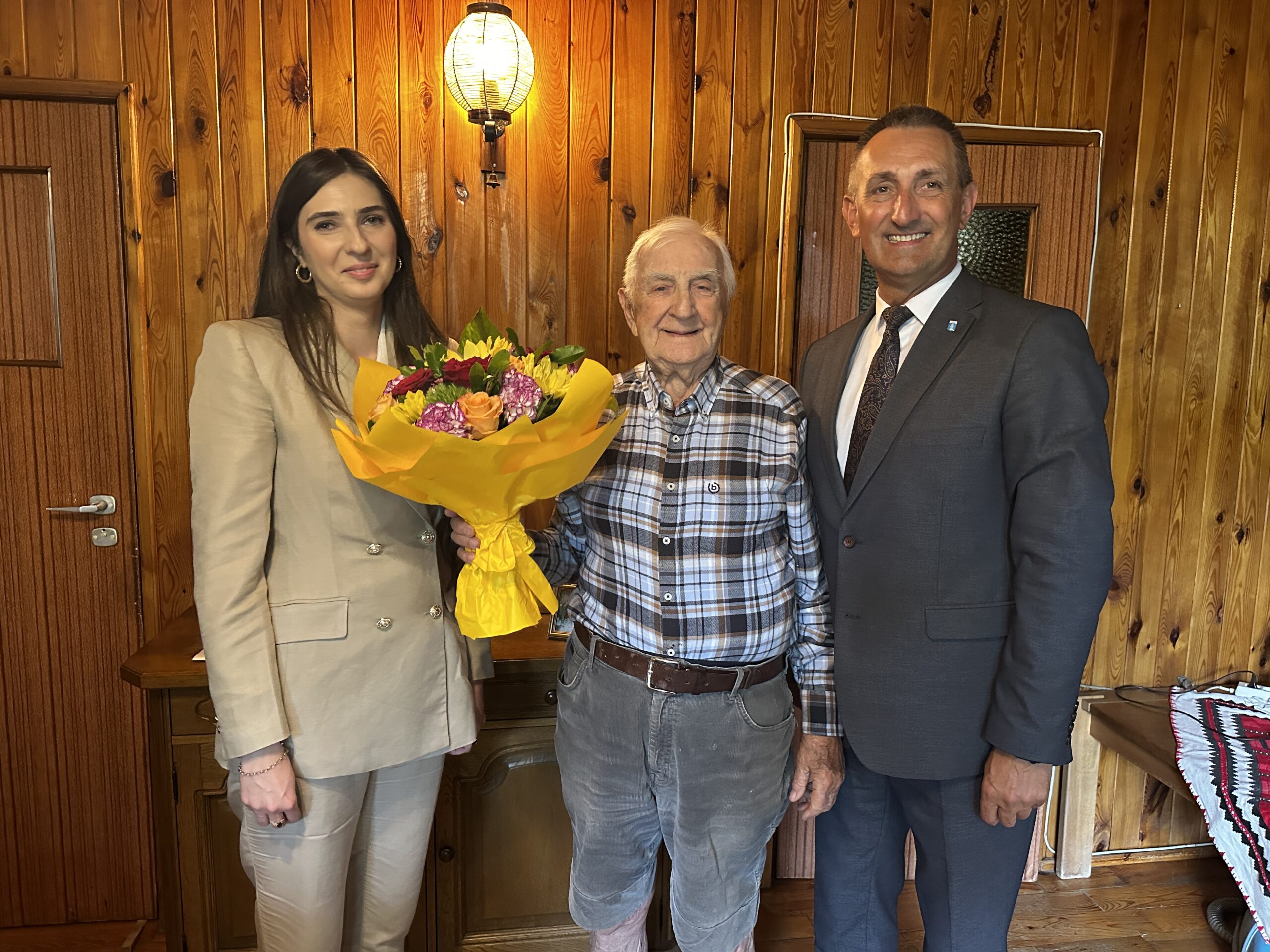 Na fotografii wójt Janusz Frąckowiak, pracownik urzędu stanu cywilnego Natalia Chomska i jubilat pan Janusz, który trzyma bukiet kwiatów.