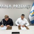 Na fotografii wójt oraz druh Rober Pawłowski podczas podpisywania umowy. W tle srebrny napis: "Gmina Przemęt" oraz flagi: Polski i Europejska.